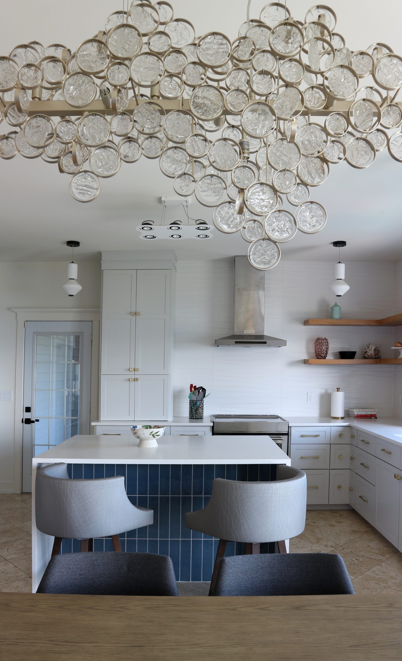 chandelier with bubble-like glass discs over dining table with light grey kitchen with waterfall edge island