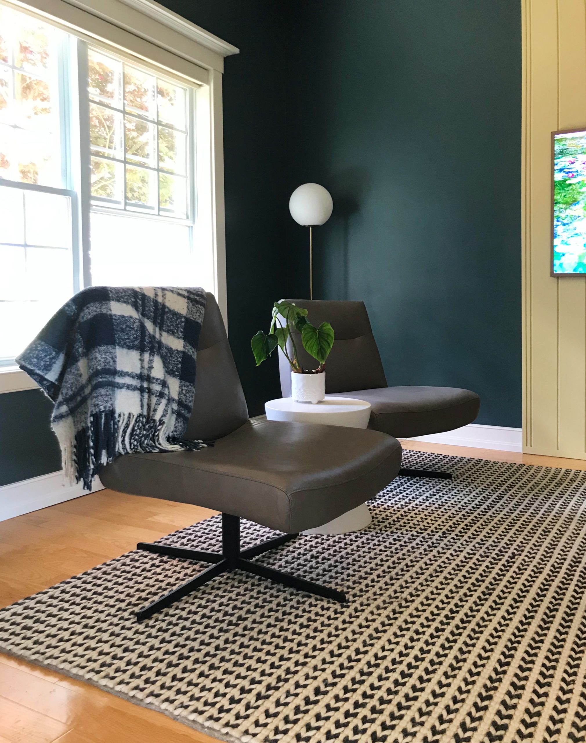 den with two swivel armless modern chairs, wool houndstooth carpet and dark teal walls and globe floor lamp